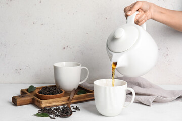 Woman pouring hot black tea into cup on table