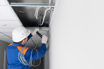 a master in a blue uniform and a white helmet, laying wiring for a WiFi router in a hidden false ceiling system, there is a place for an inscription