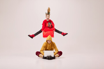 Emotional flexible young couple of ballet dancers in warm winter homewear dancing isolated on grey background. Retro, vintage, dance, holidays, party concept