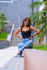 Portrait of a young brunette model in a black cap and jeans sitting in the city