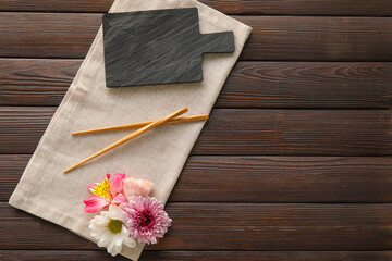 Table setting with chopsticks and flowers on dark wooden background