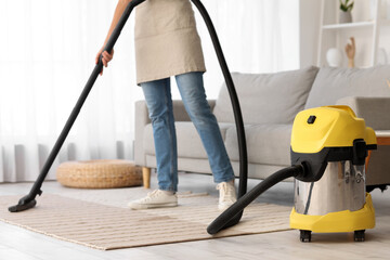 Fototapeta premium Young housewife cleaning carpet with vacuum cleaner at home