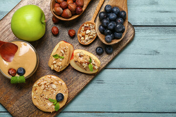 Board with tasty apples, nut butter and blueberry on color wooden background, closeup