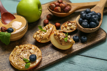 Board with tasty apples, nut butter and blueberry on color wooden background, closeup