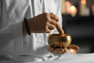 Young man with Tibetan singing bowl at home, closeup