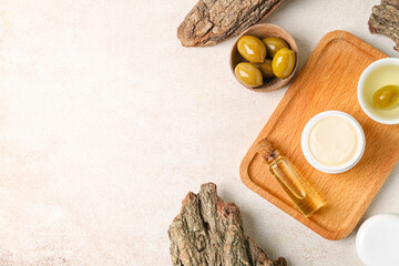 Wooden board with jar of natural olive cream and oil on light background