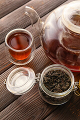 Cup and teapot of black tea and dried leaves on wooden background, closeup