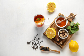 Board with glass cup of black tea, lemon, honey, mint and cane sugar on white background