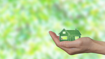 In the palm of a woman's hand, an eco-green house. Blurry green leaves in the background
