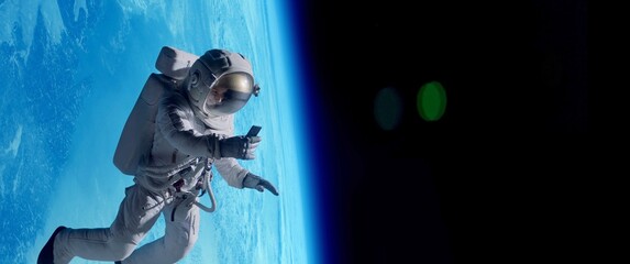Female astronaut having a video call on her phone while performing space walk in open space, Earth in the background - obrazy, fototapety, plakaty