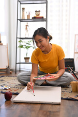 Fototapeta na wymiar Millennial beautiful woman painting picture on canvas with oil paints in bright home studio. Leisure activity and art concept