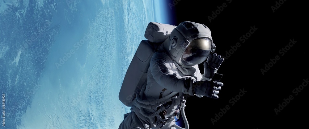 Wall mural female astronaut having a video call on her phone while performing space walk in open space, earth i