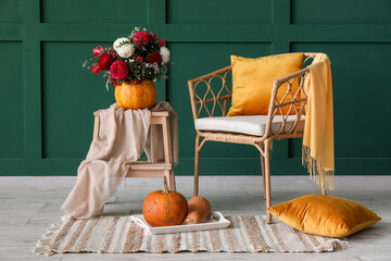 Pumpkin with beautiful flowers on stepladder, armchair and pillows near green wall
