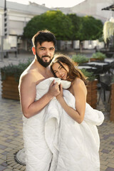 Man and a woman, in white blankets drinking tea or coffee from cups on the street in the morning.