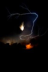 Vertical shot of flying sparks and striking lightning in a night sky
