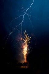 Vertical shot of fireworks exploding in a night sky while lightning strikes