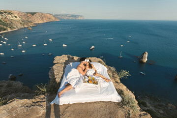 Romantic breakfast of a man and a woman in a white bed on a cliff overlooking the sea and yachts.
