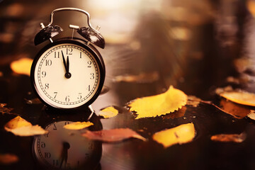 Black alarm clock on colorful maple leaves background. Closeup. Time change concept.