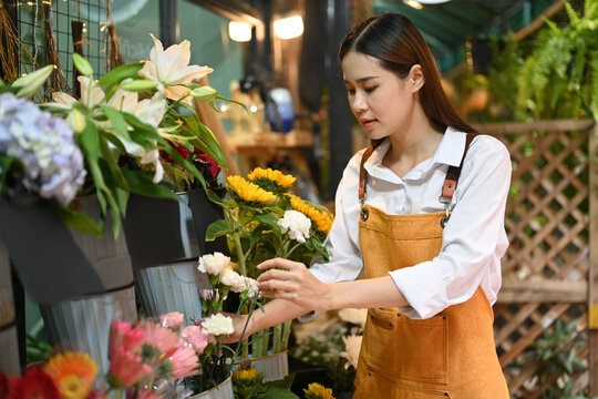 Asian woman florist wearing apron arranging flowers at her rustic flower shop. Business, sale and floristry concept