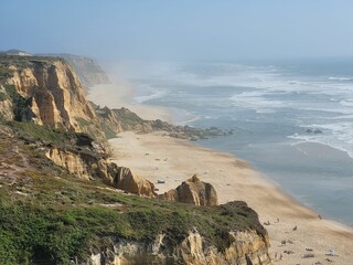 Aerial hazy view of green rocky cliffs in Praia de Vale Furado Beach in Pataias, Portugal