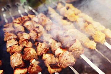 Selective focus. Cooking barbecue on the mangal in nature. Grilled tasty meet cooking on the party. Traditional Russian shashlik on a barbecue skewer on sunny forest.