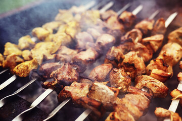 Selective focus. Cooking barbecue on the mangal in nature. Grilled tasty meet cooking on the party. Traditional Russian shashlik on a barbecue skewer on sunny forest.