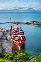 Aerial view over bright red container ship unloading at port in Napier, Hawkes Bay, New Zealand