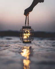 Human hand holding modern and minimalist black mesh lighted lantern above water surface © Gonçalo Lopes/Wirestock Creators