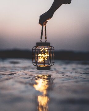 Human hand holding modern and minimalist black mesh lighted lantern above water surface