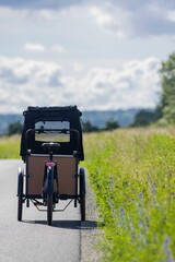 Vertical close-up of a cargo bike parked on rural road near grassy field on sunny day