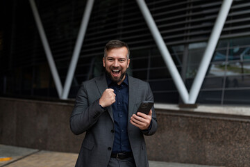 adult successful businessman after making a deal with a mobile phone in his hands with a gesture shows joy, online banking concept