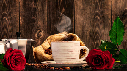 White cup of coffee with steam, coffee beans in a bag, geyser coffee maker. Composition with red roses for International Coffee Day on a dark background. View from below