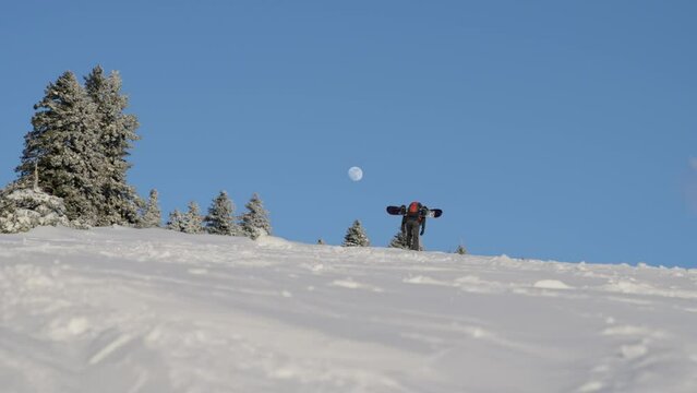 Low angle shot of a traveler with snowboard climbing on the snowy mountain