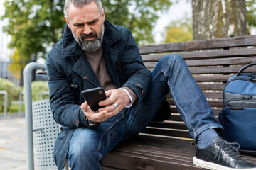 adult man sitting on a bench in the park looking at a mobile phone