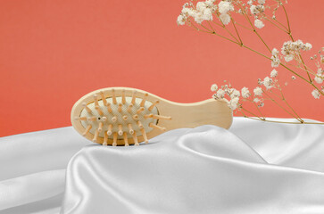 Wooden hairbrush on a podium made of silk fabric.