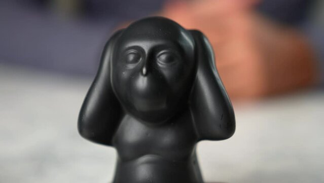 Closeup of Kikazaru monkey statue who hears no evil and a gesticulating man in the background
