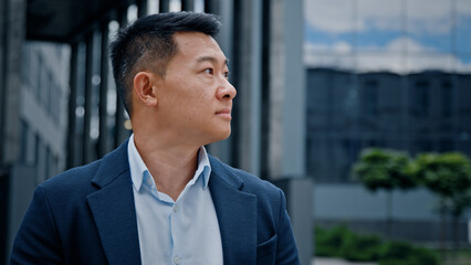 Pensive thoughtful employer look away thinking dreaming turn to camera smiling in city outdoors Asian Korean man business boss leader company CEO happy middle-aged businessman near office building