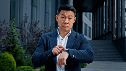 Angry worried 40s Asian businessman male frustrated boss manager CEO waiting meeting outdoors in...
