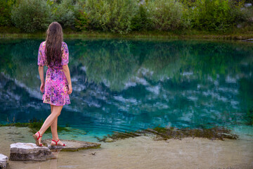 beautiful girl in a dress stands by the mysterious source of the river cetina, in which the clouds are reflected; vacation in croatia