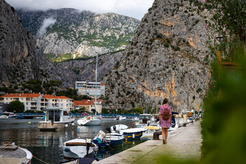 beautiful long-haired girl in a purple dress walks through the town of Omiš with a view of the...