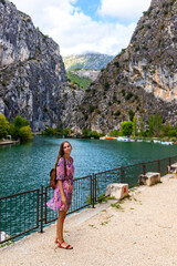 beautiful long-haired girl in a purple dress walks through the town of Omiš with a view of the cetina river and mighty mountains; croatian coast, cetina estuary, adriatic coast