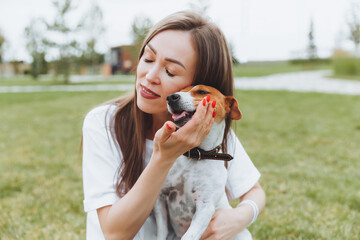 A woman in a white T-shirt and jeans hugs her Jack Russell Terrier dog in nature in the park. Loyal best friends since childhood. Lifestyle.