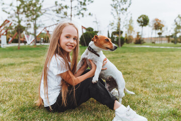 a little girl kisses and hugs her Jack Russell terrier dog in the park. Love between the owner and...