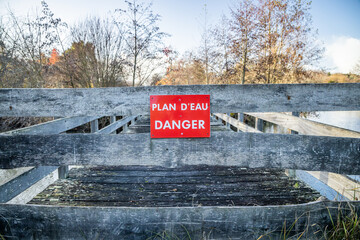 "Body of water, danger" French sign on the wooden fence of a bridge