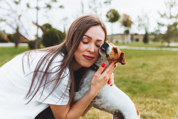 A woman in a white T-shirt and jeans hugs her Jack Russell Terrier dog in nature in the park. Loyal best friends since childhood. Lifestyle.