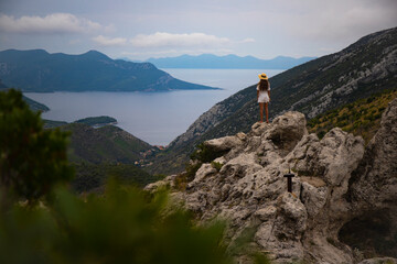 a beautiful girl in a white dress stands on a hill gazing at the panorama of the peljesac peninsula in croatia, mighty mountains and cliffs over the mediterranean sea