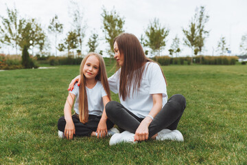 A happy mother and her daughter are sitting on the grass in the park and hugging. mother and daughter. family.joyful mom and little girl