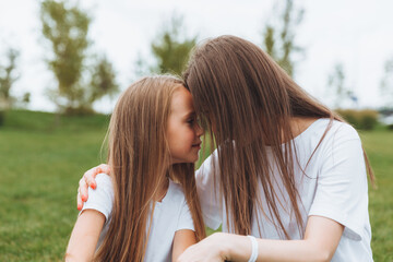 Fototapeta premium A happy mother and her daughter are sitting on the grass in the park and hugging. mother and daughter. family.joyful mom and little girl