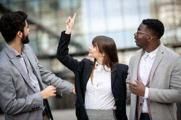 Three succesfull business people talking to each other and smiling other during meeting in the city. Using mobile. Mixed race