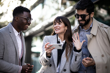 Three business people talking to each other and smiling other during meeting in the city. Using mobile. Mixed race
